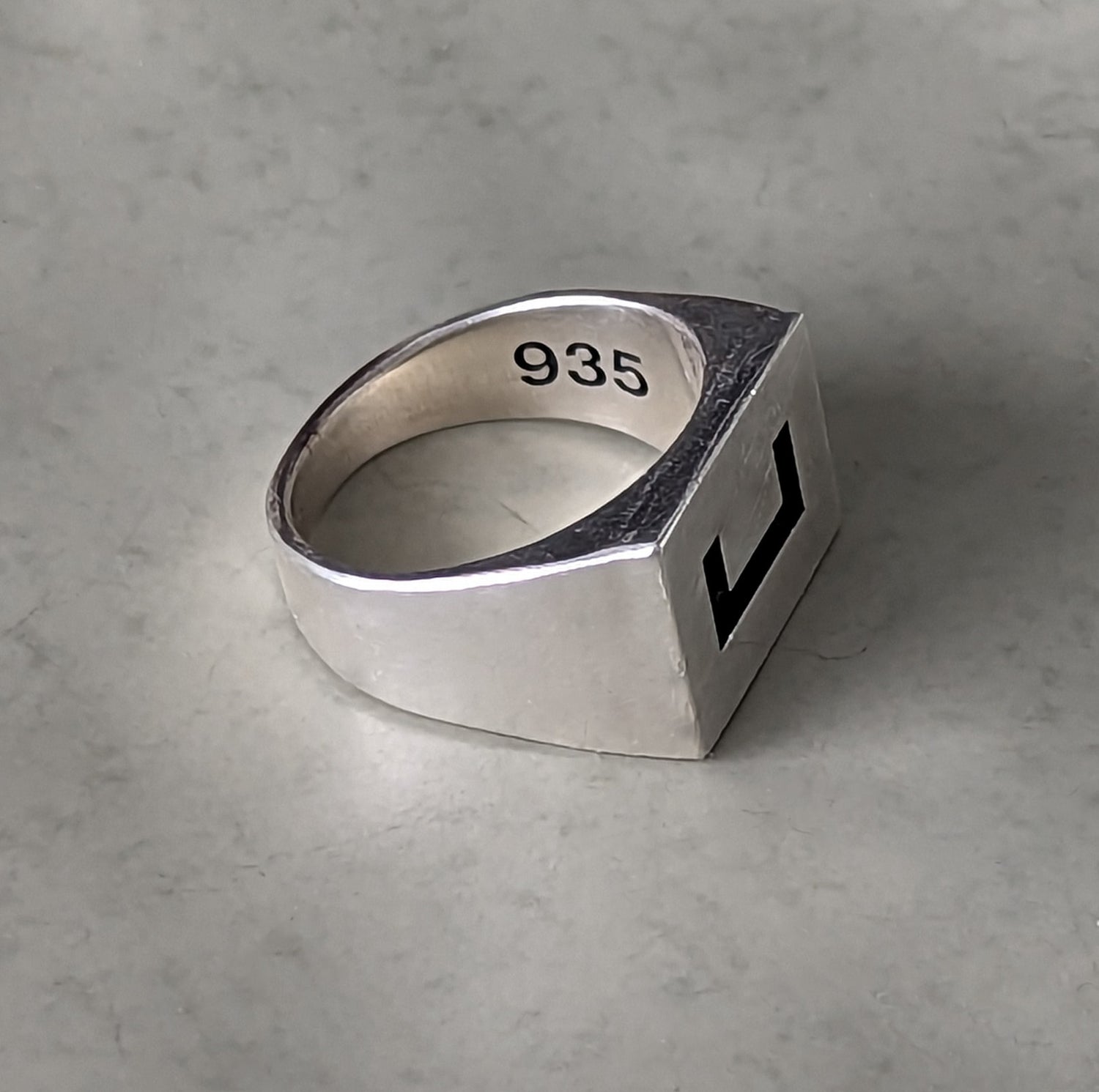 Closeup image of brilliant 935 silver showcasing 935 engraved and oxidized for contrast, alongside the front face of the rectangle knuckle with a bold single square bracket in the middle also engraved and oxidized.