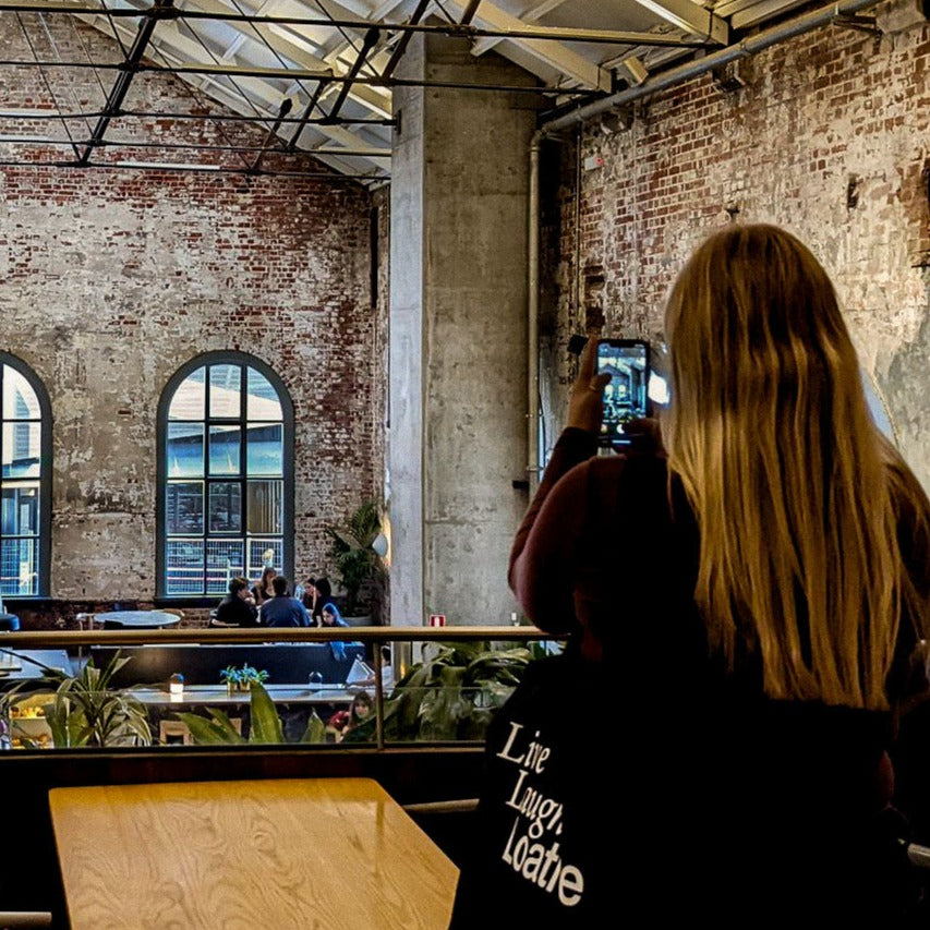Showcasing the oversized cotton Tote over shoulder while taking photo inside an exposed brick building